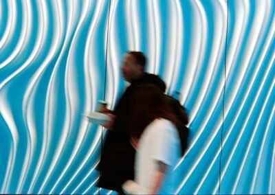 People walk past a wavy blue and white illuminated wall